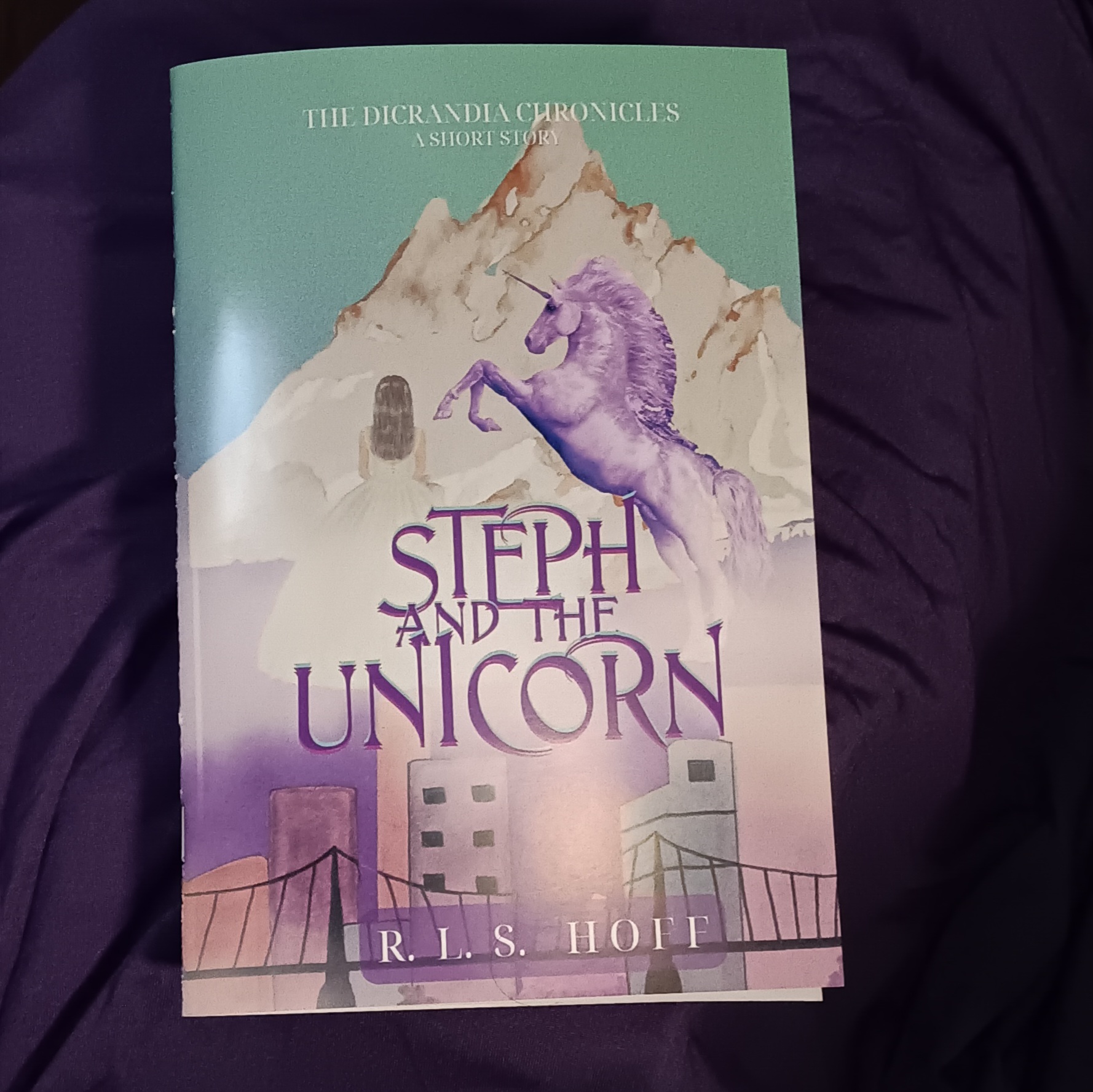 A glossy bound zine copy of Steph and the Unicorn sits on a purple background.