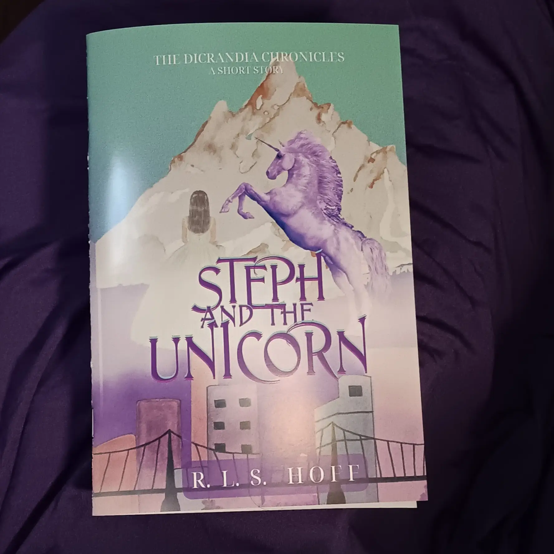 A glossy bound zine copy of Steph and the Unicorn sits on a purple background.